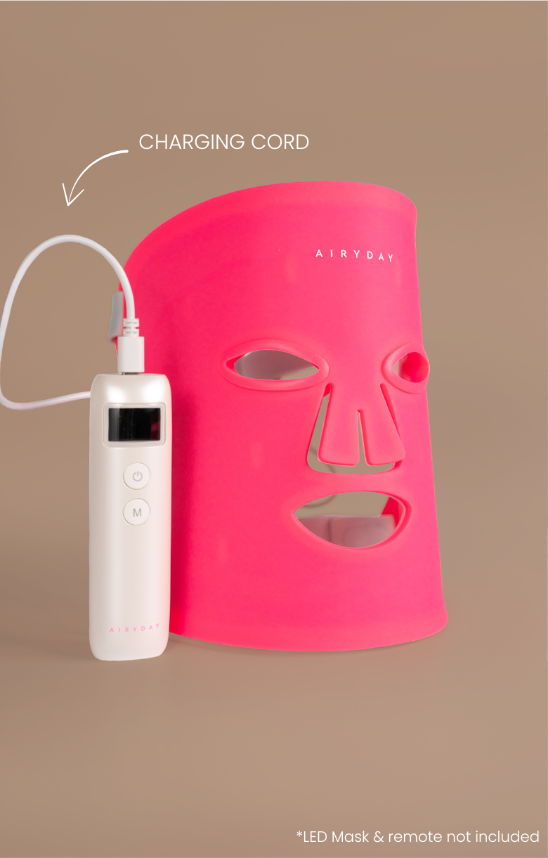 Pink LED face mask with white charging remote on a brown background