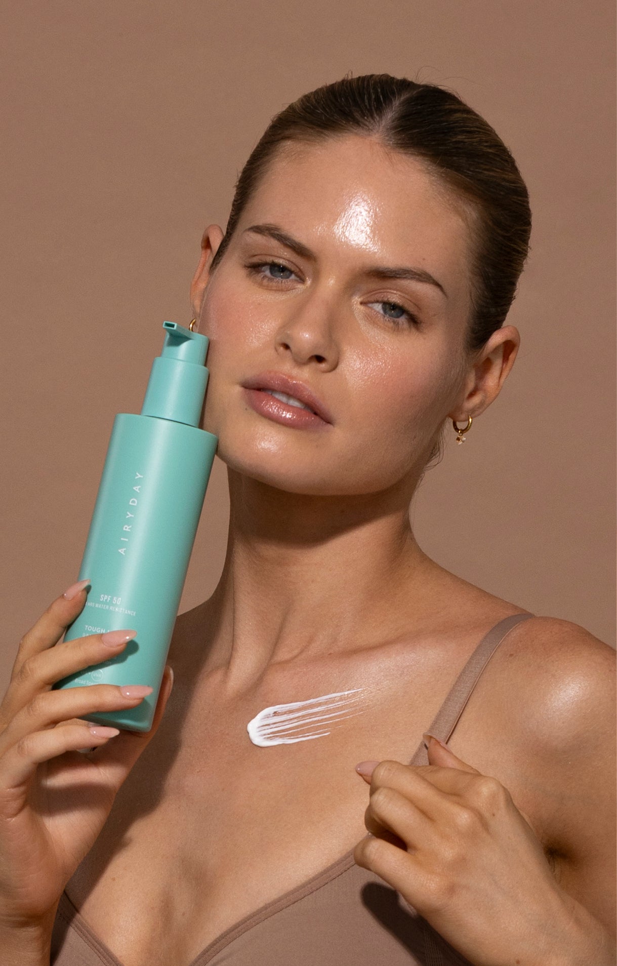 Model applying sunscreen to her shoulder with a bottle of Airyday Tough Luxe SPF50